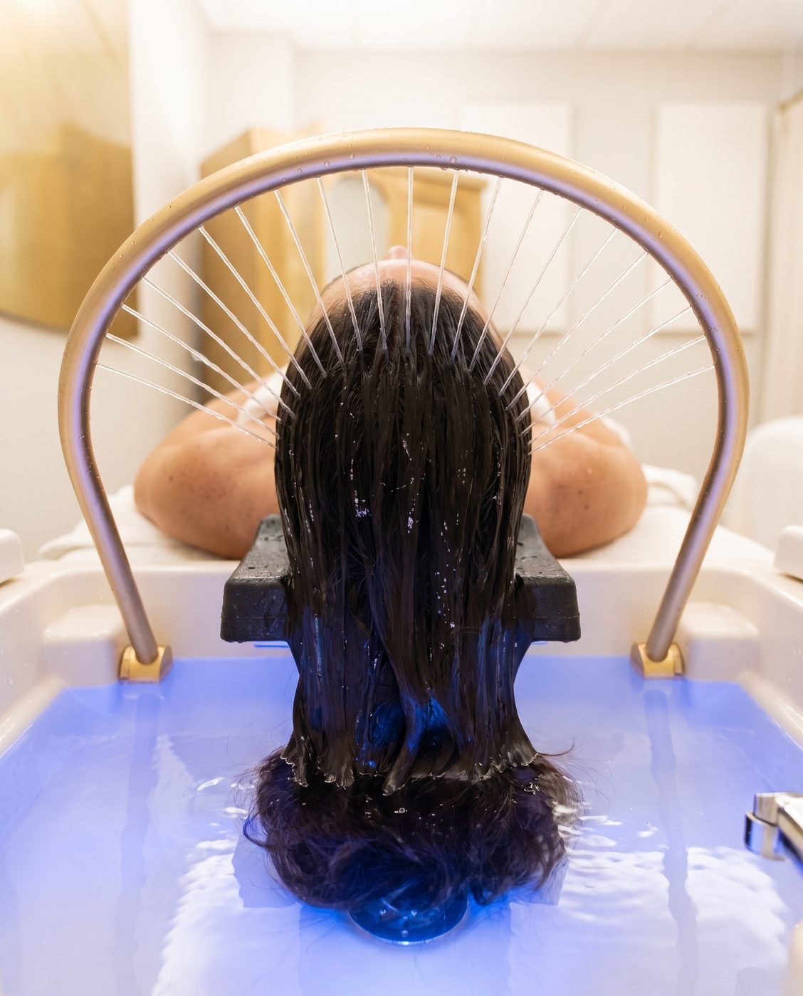 Water arch rinsing hair over a softly lit basin